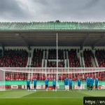 Home 19 벨라루스 축구 리그 소개 - A dynamic scene of a Belarusian football match in a modest stadium with passionate local fans waving...